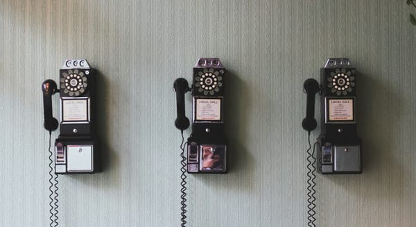 Three rotary pay-phones next to each other attached to a wallpapered wall.